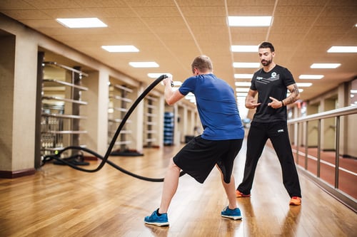 person using battle ropes with personal training assisting