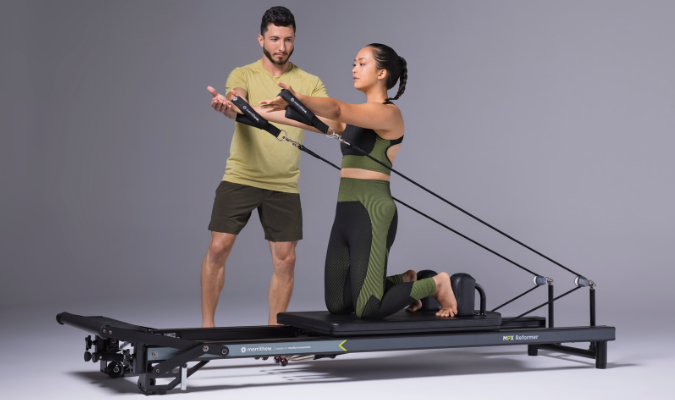 Woman on Pilates reformer getting help from instructor